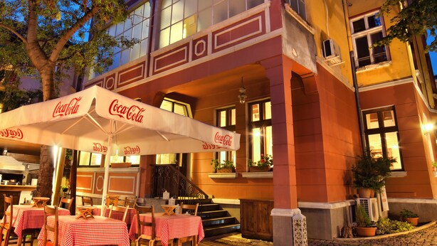 Un edificio de dos pisos con mesas al aire libre y sombrillas con la marca Coca-Cola.