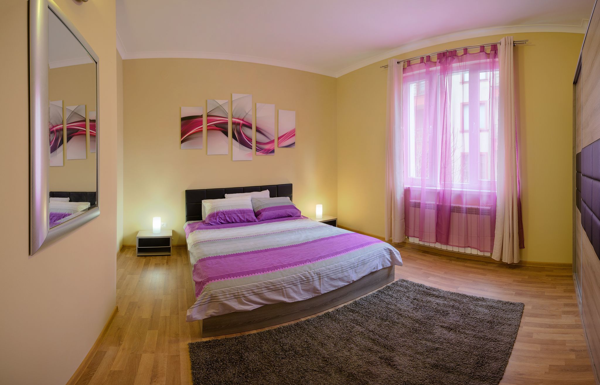 Un dormitorio con cama, mesita de noche, espejo y obras de arte en la pared.