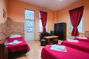 A hotel room with two beds, a small table, a black chair, a wooden wall feature, and a window with a stained glass design. - Guest House 32 (Sofia)