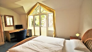 Une chambre à coucher comprenant un lit, un bureau, une chaise, un téléviseur et une fenêtre avec des rideaux.