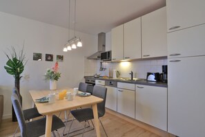 Een moderne keuken met witte kasten, een magnetron, een koffiezetapparaat en een eettafel met stoelen.