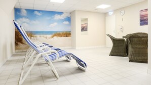 A room with a beach mural, reclining chairs, and wicker furniture. - Haffblick Whg. Ha31, Germany (Ostseebad Boltenhagen)