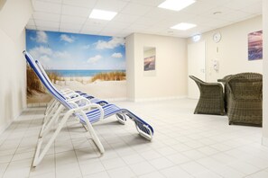 Une pièce décorée d’une fresque représentant une plage, avec des fauteuils inclinables et des meubles en osier.
