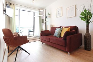 Una sala de estar con un sofá rojo, un sillón marrón y una planta grande.