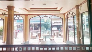 A spacious indoor area with large glass windows, wooden columns, and a balcony with outdoor seating. - Hua Lin Inn (Chiang Mai)
