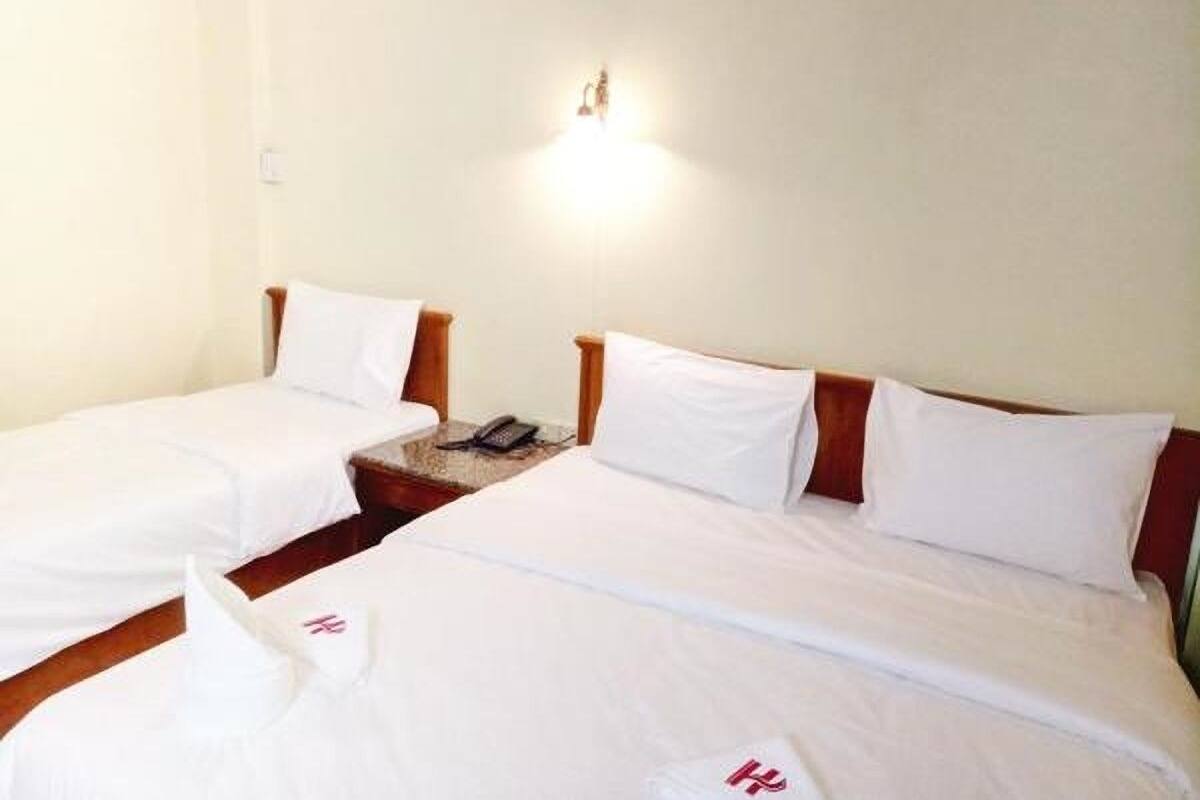 Quarto de hotel com duas camas de solteiro, mesa de cabeceira com telefone e luminária na parede.