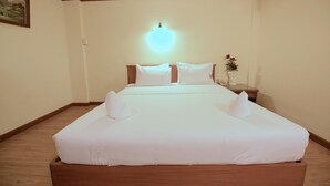 A hotel room with a large bed, a nightstand with a vase of flowers, and a painting on the wall. - Hua Lin Inn (Chiang Mai)