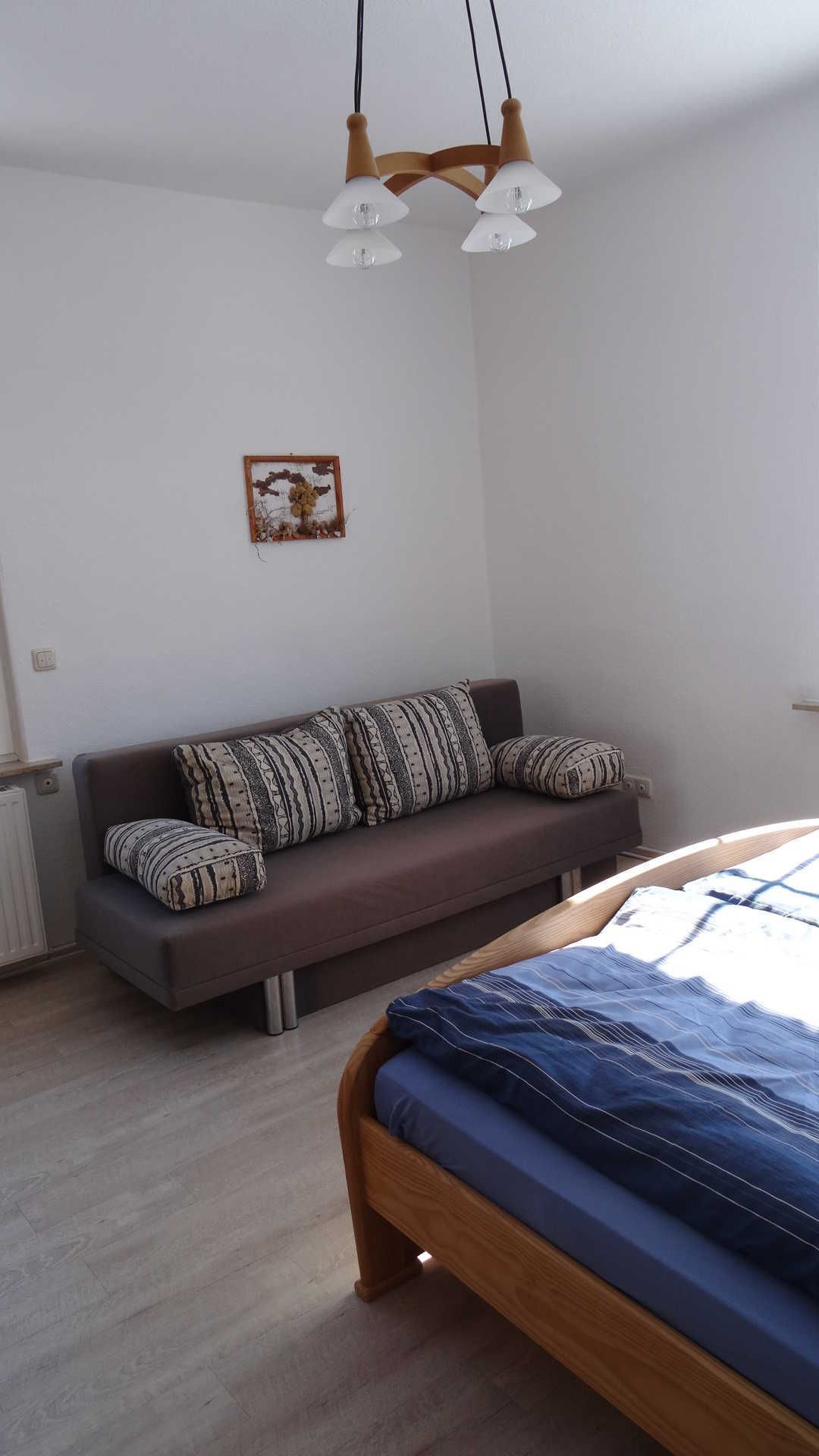 A bedroom with a bed, a sofa, and a hanging light fixture.
