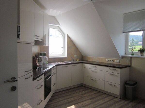 A modern kitchen with white cabinets, a built-in oven, and a window providing natural light.