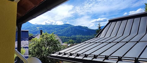 A view from a balcony with a mountain backdrop, a satellite dish, and a building with a sloped roof.