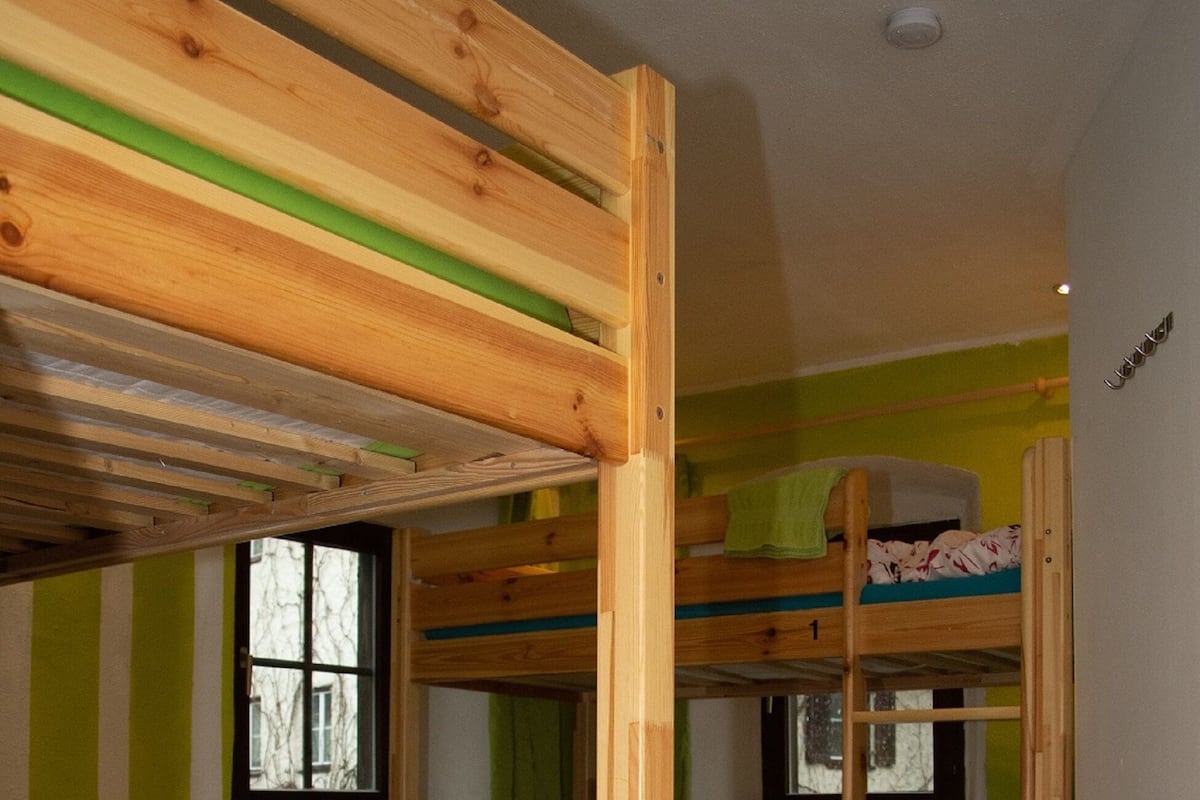 A bunk bed room with a table and chairs, a window, and a trash bin.