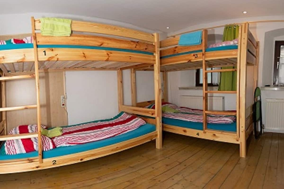 A bunk bed room with a small table and chairs, a radiator, and a window with curtains.