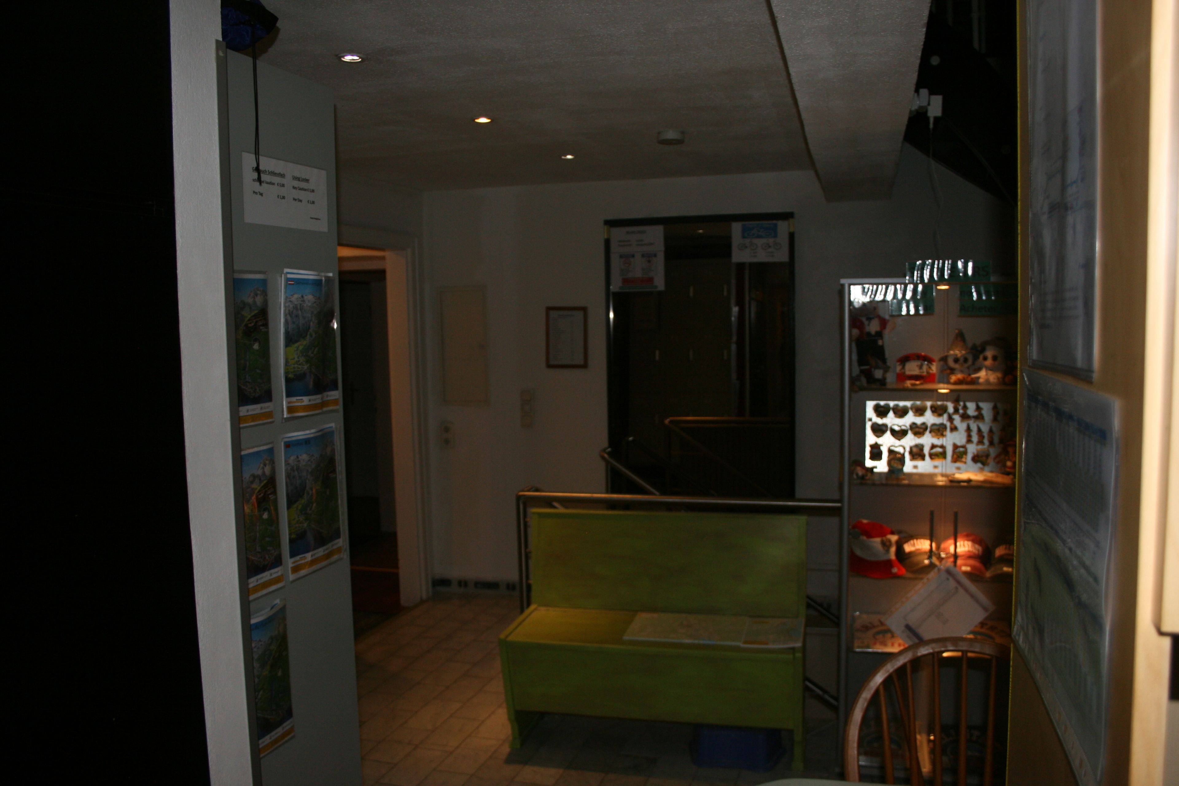 Un pasillo estrecho con un banco verde, un refrigerador con varios artículos y una puerta que da a otra habitación.