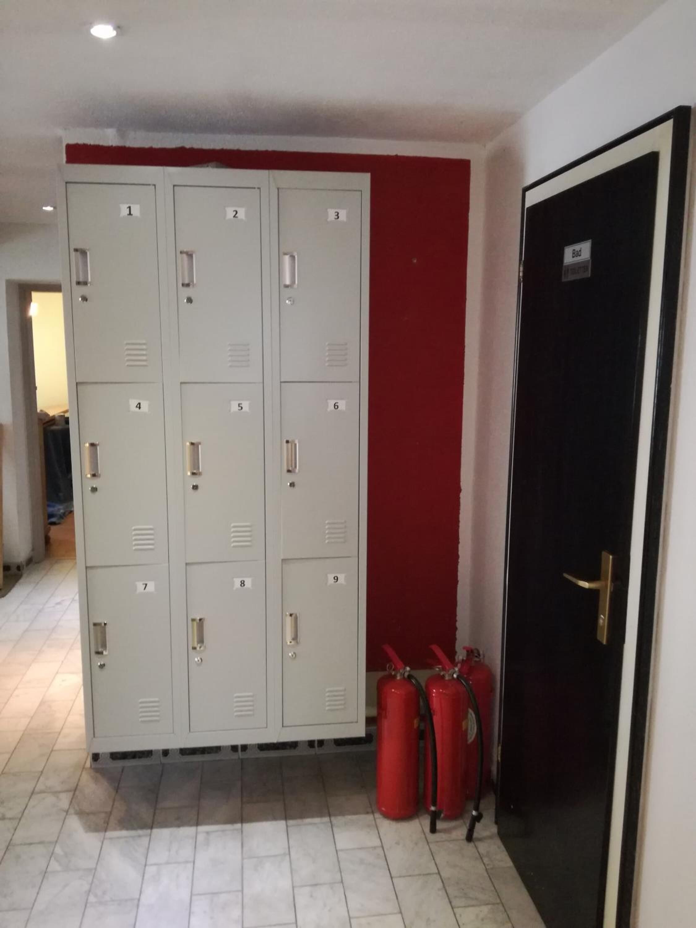 A hallway with lockers numbered 1 to 9, a black door labeled "Bad," and two red fire extinguishers.