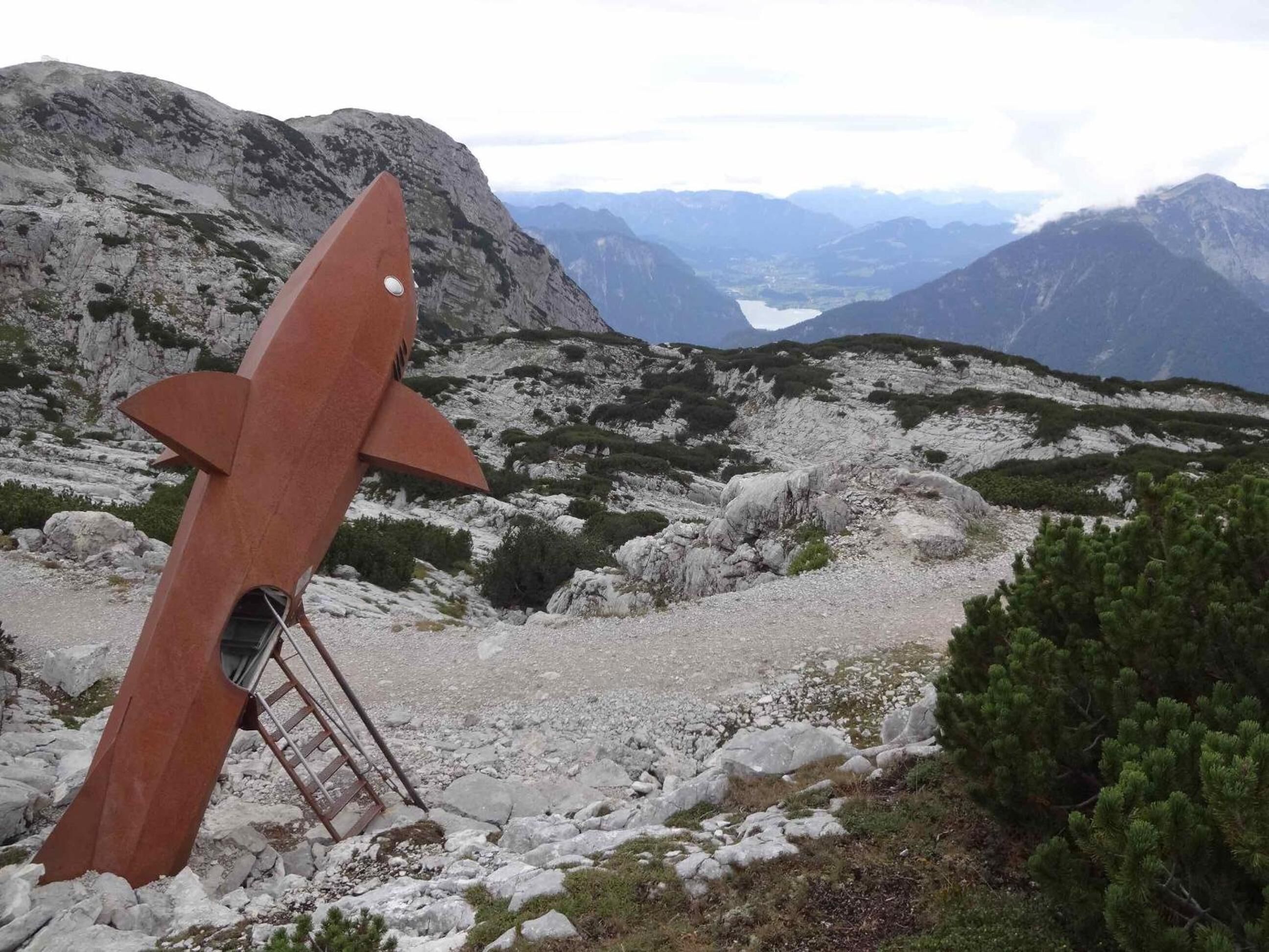 Een ruig berglandschap met een grote metalen sculptuur die op een raket lijkt.