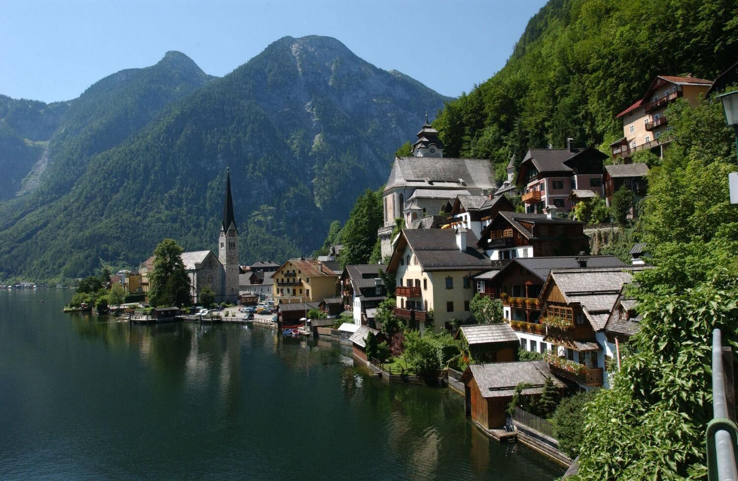 A lakeside village with traditional wooden houses, a church, and mountains in the background.