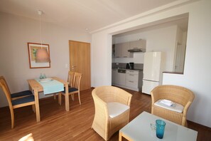 A room with a dining table, chairs, a small kitchen area, and wicker furniture.