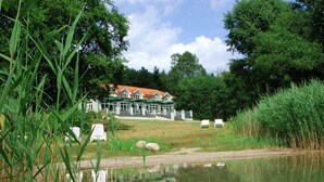 A lakeside hotel with a large building, outdoor seating, and a pond.