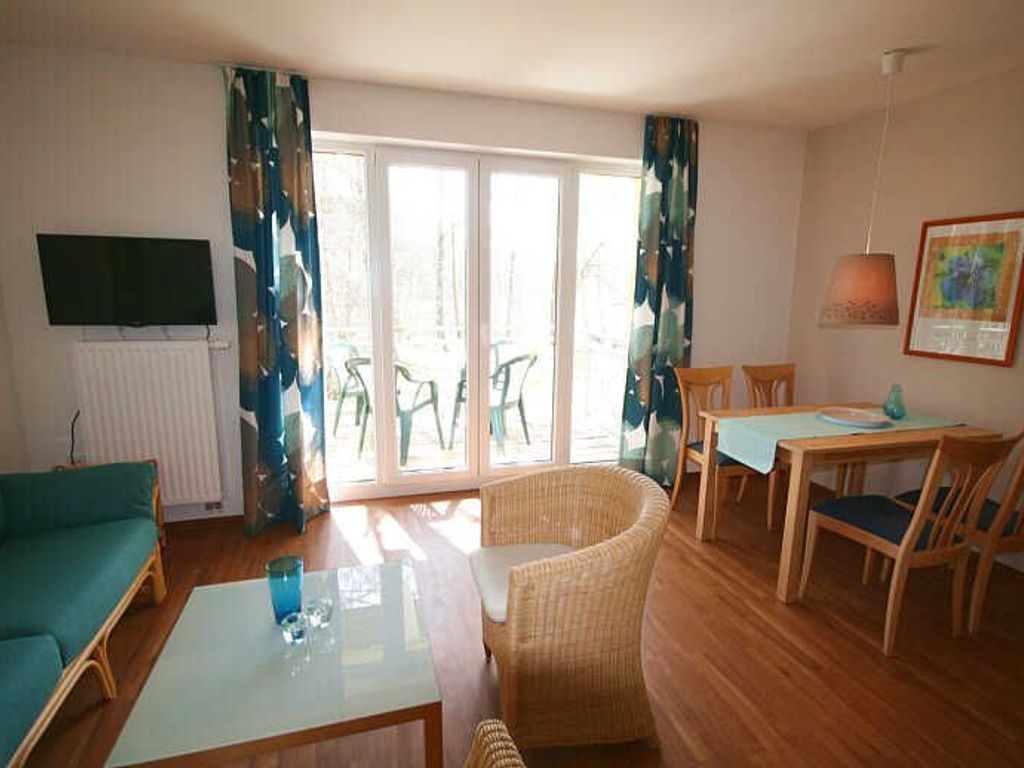 A room with a sofa, a dining table with chairs, a TV mounted on the wall, and a window with curtains.