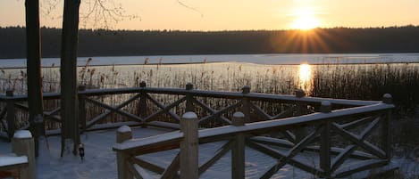A wooden deck with railings overlooking a frozen lake at sunset.