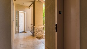 Un pasillo con un pilar de piedra, una puerta blanca y un número que indica la habitación.