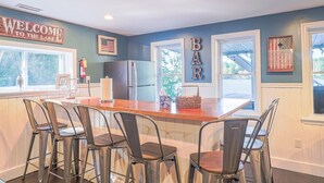 A kitchen with a bar area, featuring a wooden island with chairs, a refrigerator, and a welcome sign. - Lakefront Lookout- Hot tub- Fireplace- Dock- Bar/Game Room (Fort Ann)
