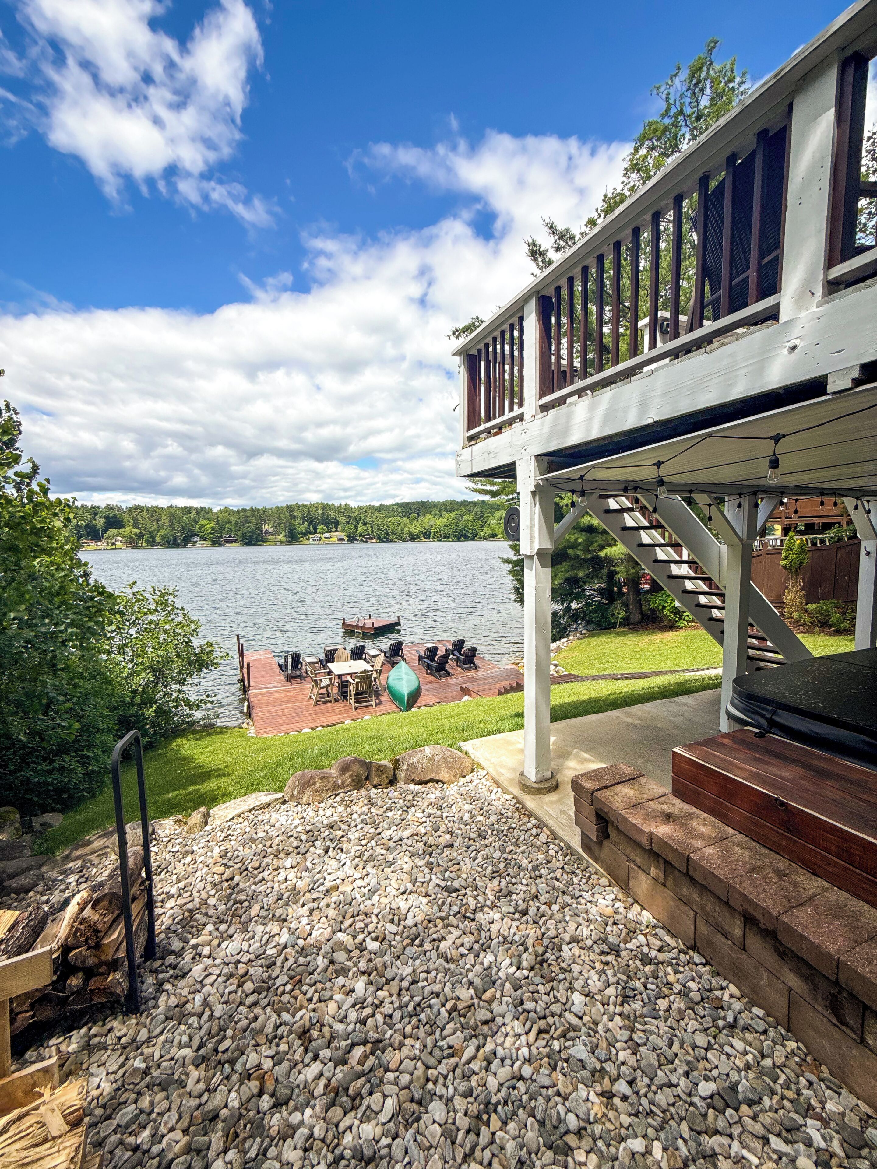 A deck with outdoor furniture overlooking a lake, a wooden staircase, and a clear sky.