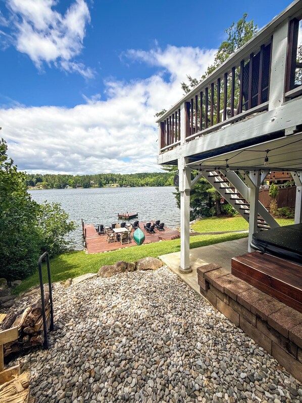 Terraza con mobiliario exterior con vista a un lago, una escalera de madera y un cielo despejado.
