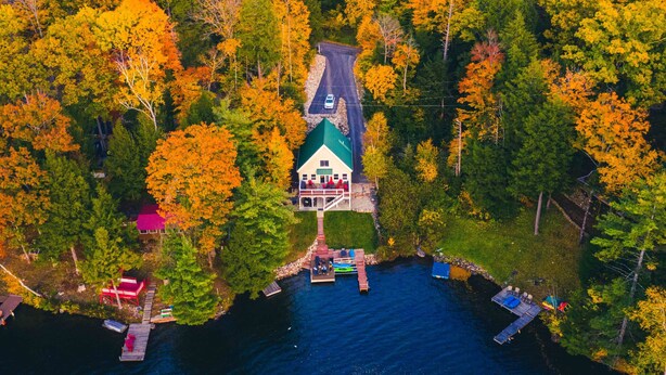 An aerial view of a house surrounded by autumn foliage, connected to a dock with boats. - Lakefront Lookout- Hot tub- Fireplace- Dock- Bar/Game Room (Fort Ann)