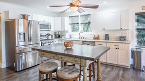 A modern kitchen with stainless steel appliances, a wooden island with stools, and a ceiling fan. - Lakefront Lookout- Hot tub- Fireplace- Dock- Bar/Game Room (Fort Ann)