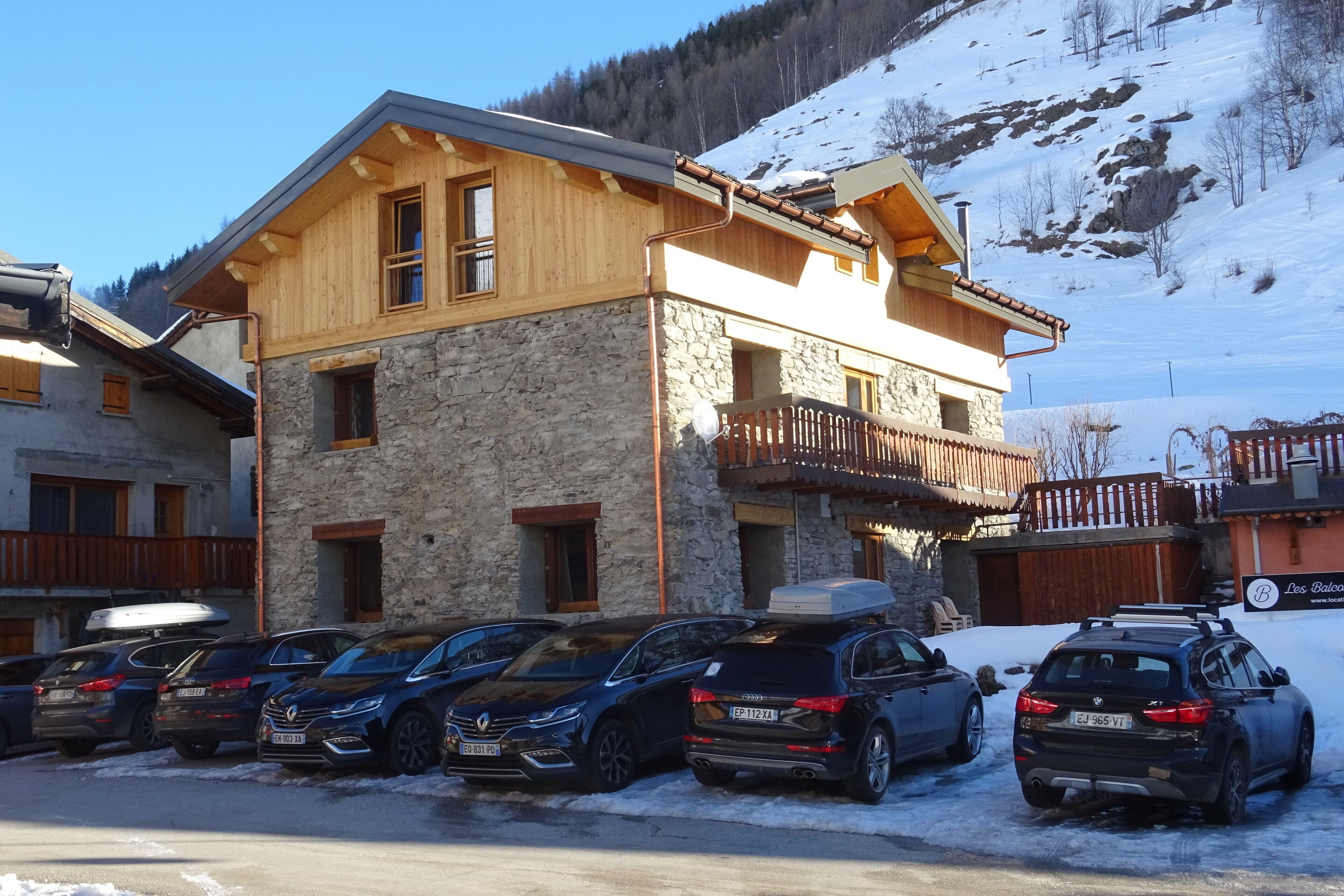 A two-story building with a stone facade and wooden upper levels, parking in front.