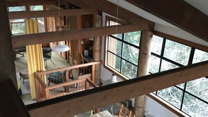 Een meerlaags houten interieur met een eetgedeelte beneden en een zithoek boven, verbonden door een houten trap.