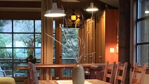 Een houten eettafel met stoelen, hanglampen en een vaas met takken.