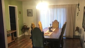 Un comedor con una mesa y sillas de madera, una araña y un ventanal con cortinas.