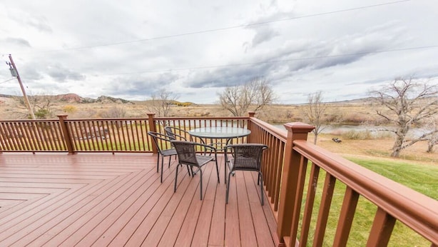 Una terraza de madera con mesa y sillas, con vista a un paisaje natural.