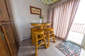 Una zona de menjador amb una taula rodona i quatre tamborets de fusta, un quadre amb una imatge de peix a la paret i una catifa estampada a prop de l'entrada.