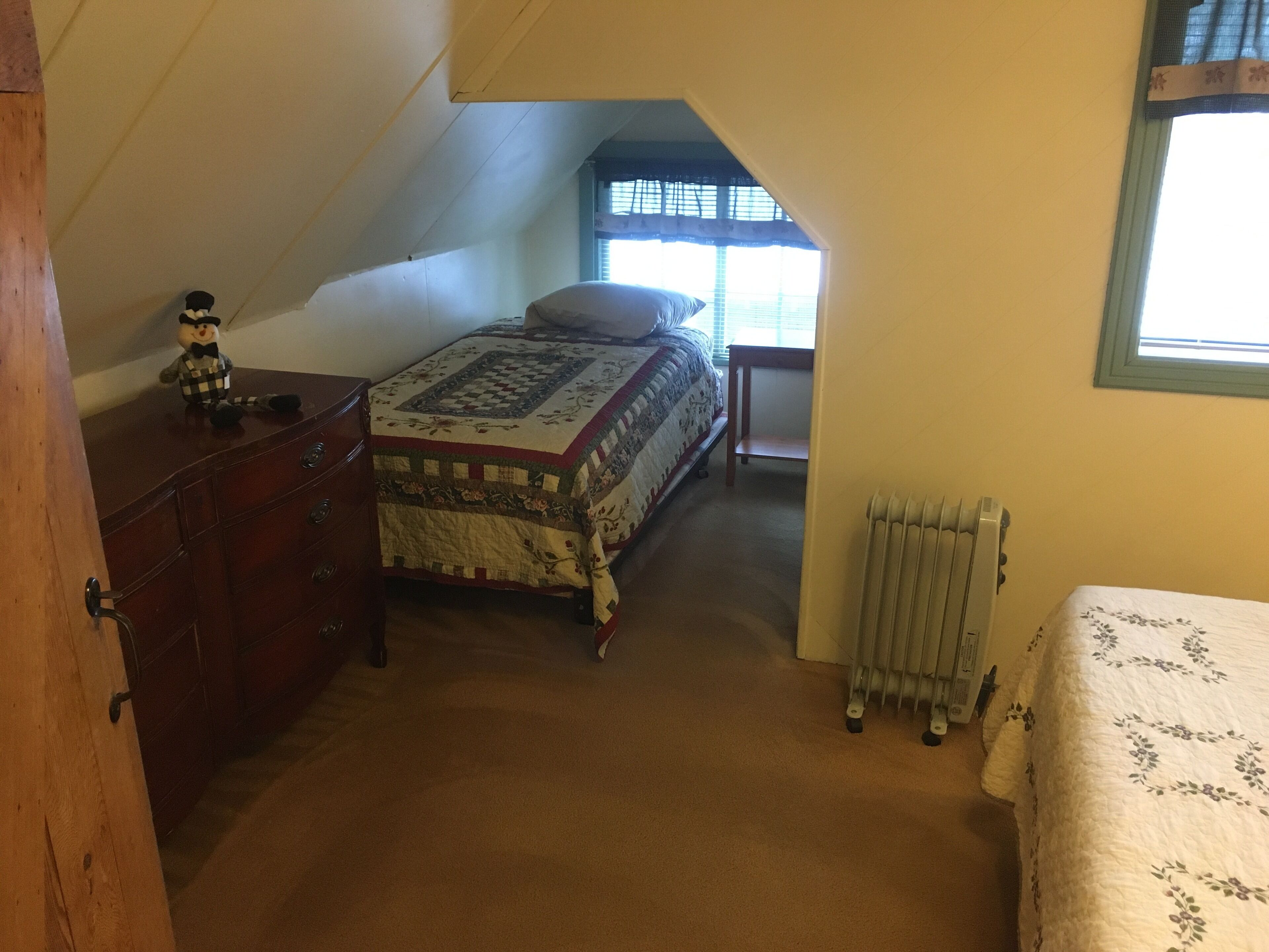 Un dormitorio con cama, cómoda, radiador y ventana con persianas.