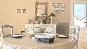 Een eetgedeelte met een ronde tafel, witte stoelen, een witte kast met decoratieve items, een visdecoratie aan de muur en een 'RE' bord.