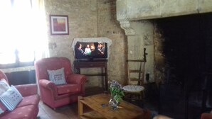 A living room with a red armchair, a wooden coffee table with a vase, a television on a stand, and a fireplace. - Very typical house LOT (Périgord-Quercy) close communal pool + Trade (Lavercantière)