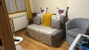 A cozy living room with a sofa, a grey armchair, a small white table, and a radiator. - Apartment in house, ALL COMFORT (Prémanon)