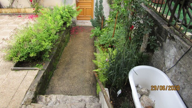 A narrow garden path leading to a wooden door, surrounded by lush greenery and potted plants. - Apartment in house, ALL COMFORT (Prémanon)