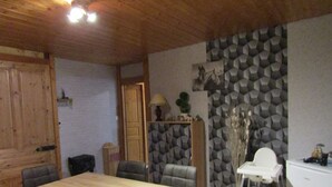 A dining area with a wooden table and chairs, a white refrigerator, and a patterned wall. - Apartment in house, ALL COMFORT (Prémanon)