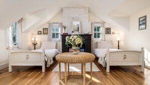 A cozy attic bedroom with two white beds, a central wicker table, and a fireplace. - Make lifelong memories at this New England Quintessential Country Getaway (Brookfield)