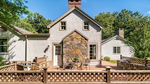 A two-story house with a stone facade, a wooden deck, and a fenced patio area. - Make lifelong memories at this New England Quintessential Country Getaway (Brookfield)