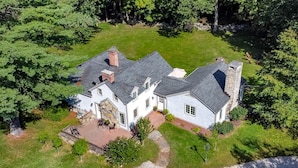 A large, two-story house with a stone chimney, surrounded by a well-maintained lawn and trees. - Make lifelong memories at this New England Quintessential Country Getaway (Brookfield)