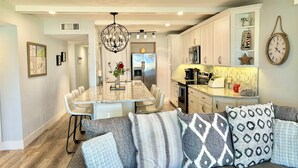 A modern kitchen with white cabinets, a central island, and a dining area with a chandelier. - Beautifully Updated Ground Floor Condo, Direct OCEAN Front on NO-DRIVE Beach! (New Smyrna Beach)