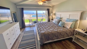 A bedroom with a large bed, a ceiling fan, a view of the ocean, a TV, and a dresser. - Beautifully Updated Ground Floor Condo, Direct OCEAN Front on NO-DRIVE Beach! (New Smyrna Beach)