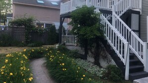Une maison avec un porche à l’avant, un escalier et un jardin où poussent des fleurs jaunes.