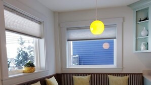 Un coin salon avec des sièges disposés en cercle autour d’une table ronde, un luminaire suspendu et une fenêtre avec des stores.
