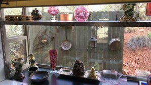 Ein Fenster mit verschiedenen Dekorationen, darunter ein Keramiktopf, eine Glasvase und eine kleine Figur.